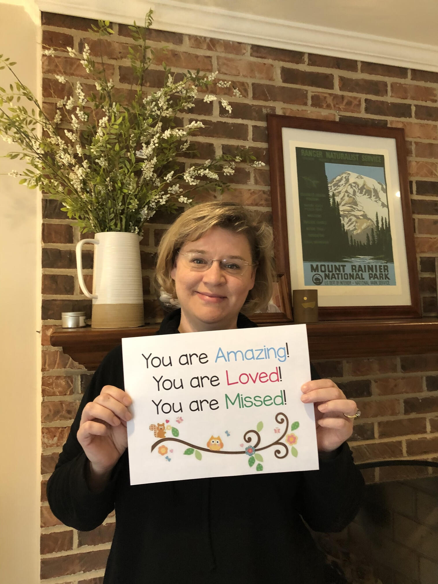 Jennifer holding a sign she made for her students during covid lockdown, which says You Are Amazing, You Are Loved, You Are Missed
