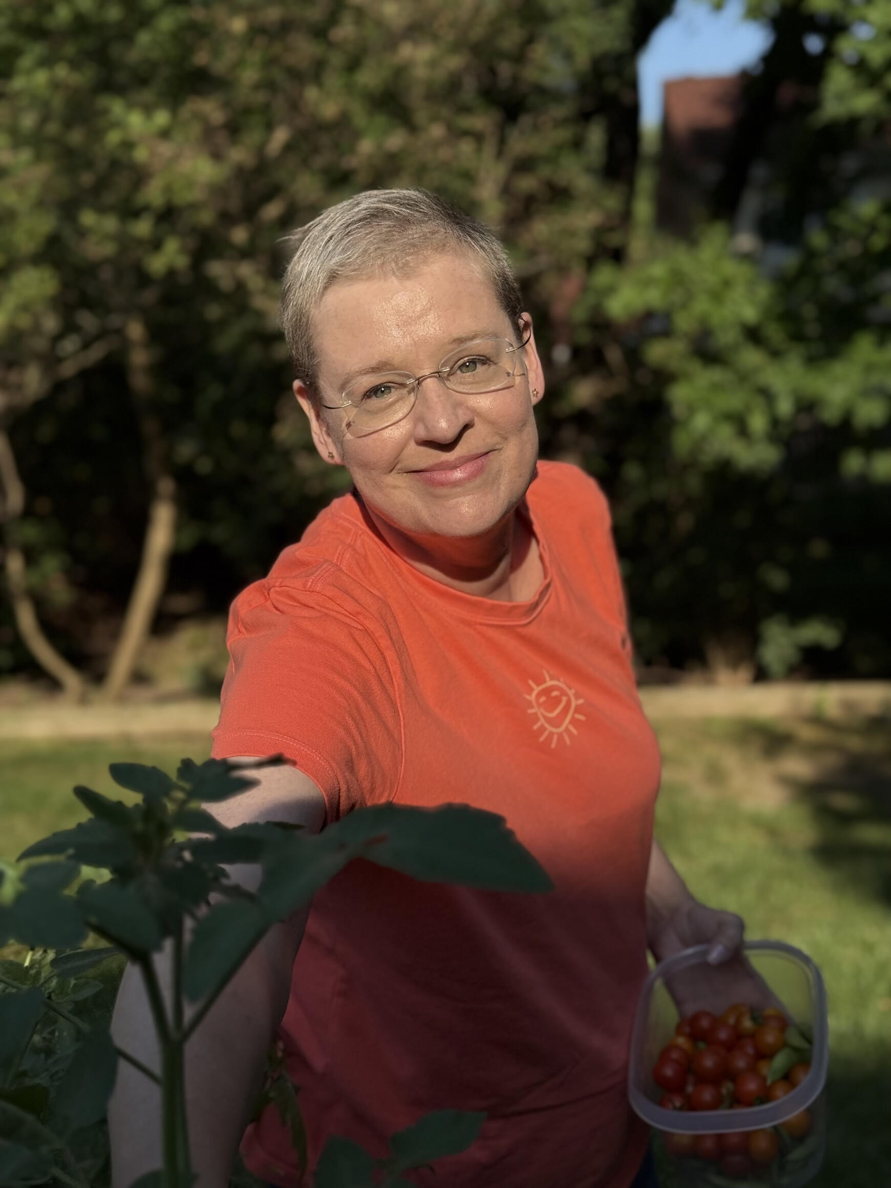 Jennifer standing in a beam of sunlight, picking tomatoes from her garden and wearing an orange t-shirt
